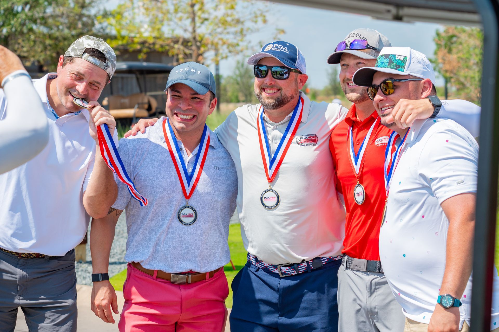 Four medal-winning athletes pose outdoors, smiling and holding up drinks in a celebratory group photo.