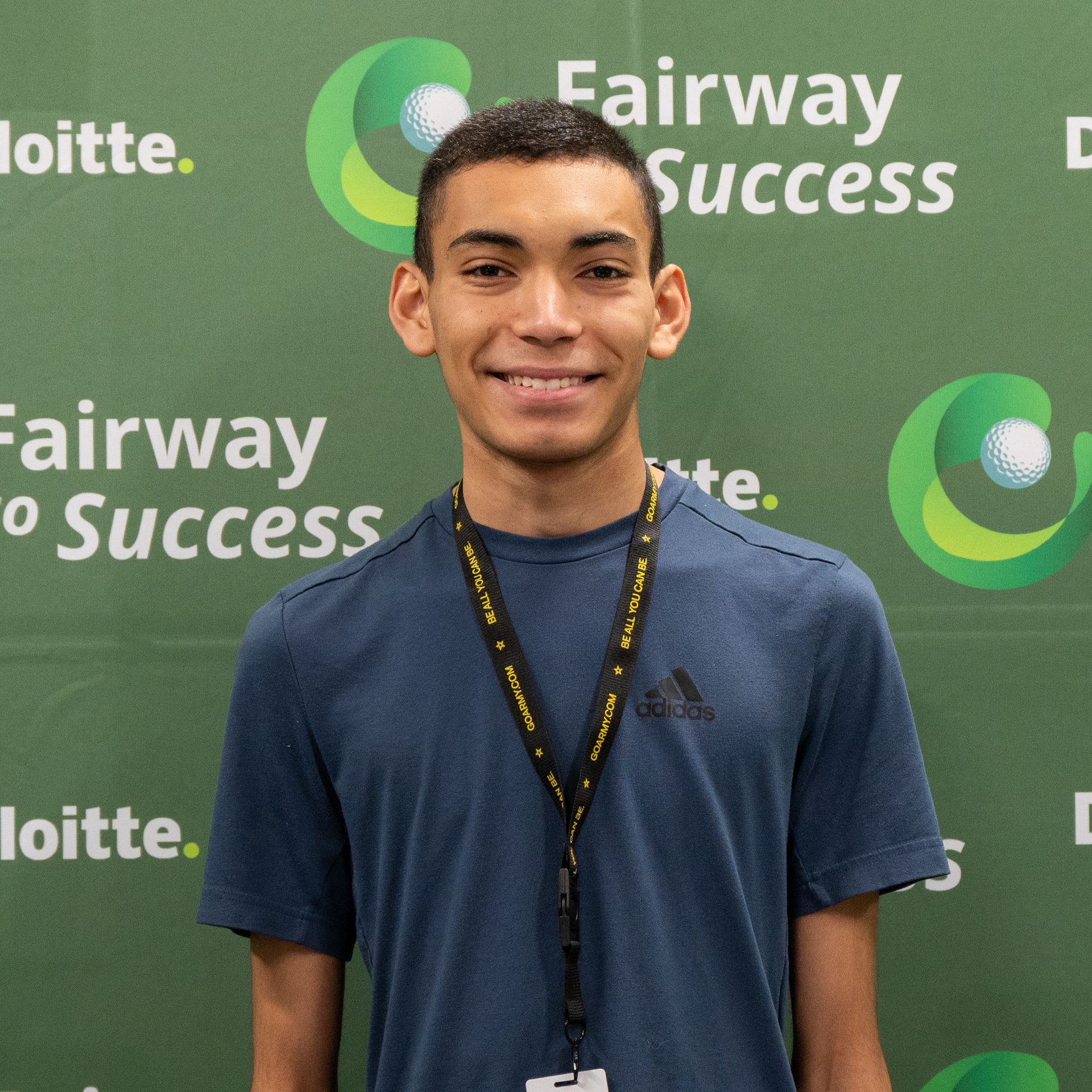 Smiling man in navy shirt and lanyard standing before a green Deloitte Fairway to Success backdrop