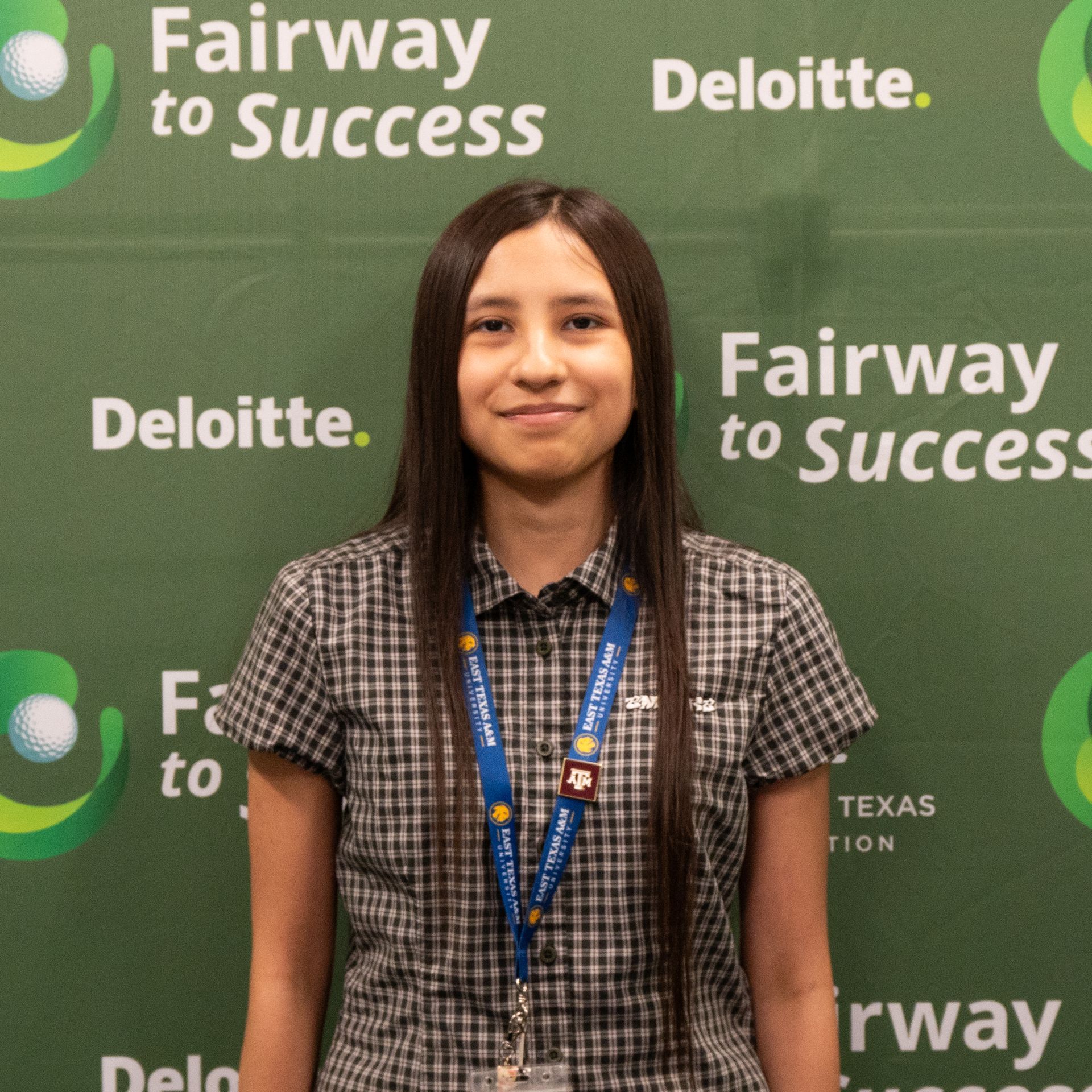 Teen standing in front of a Fairway to Success and Deloitte backdrop, smiling at the camera.