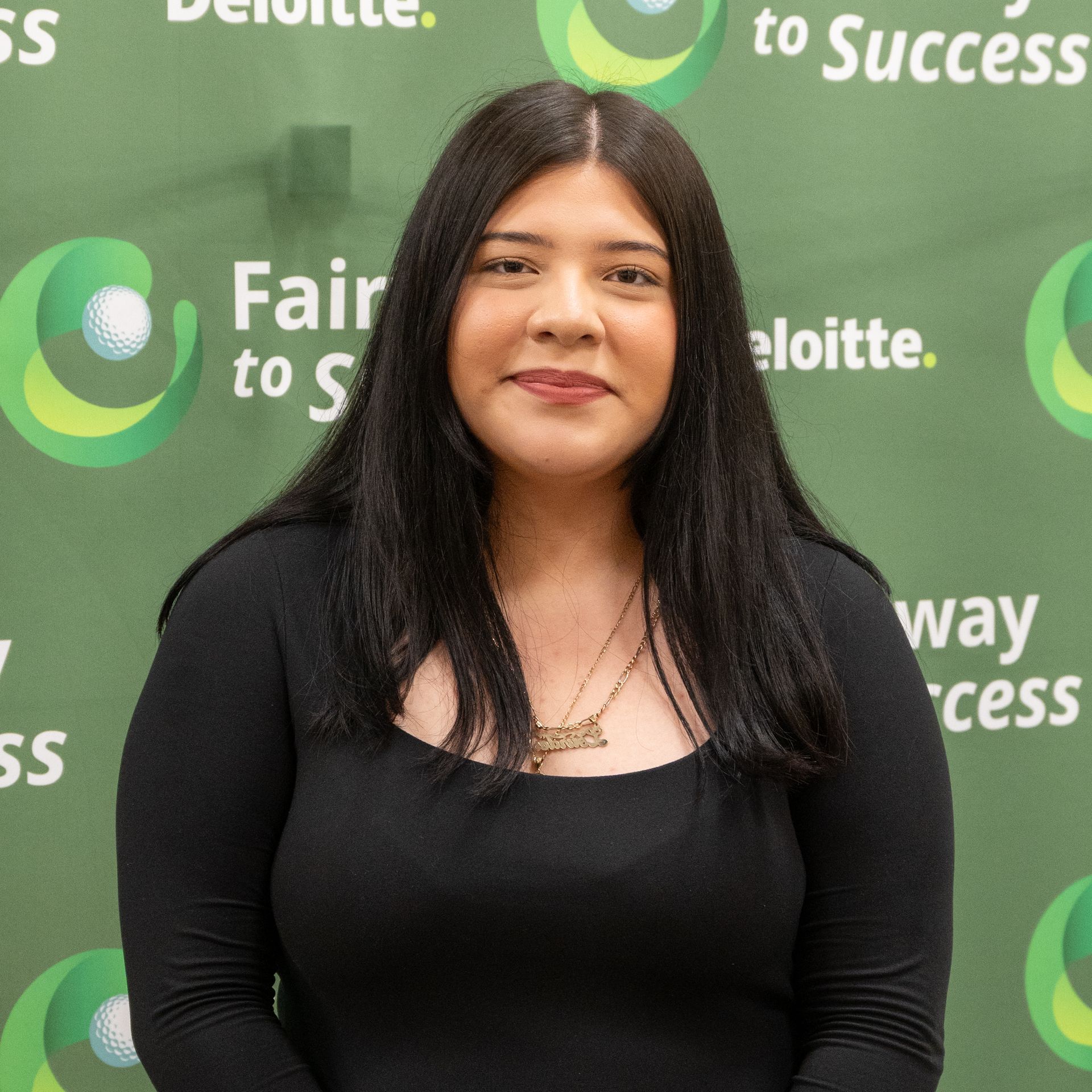 Woman in a black top standing before a green Deloitte “Pathway to Success” backdrop