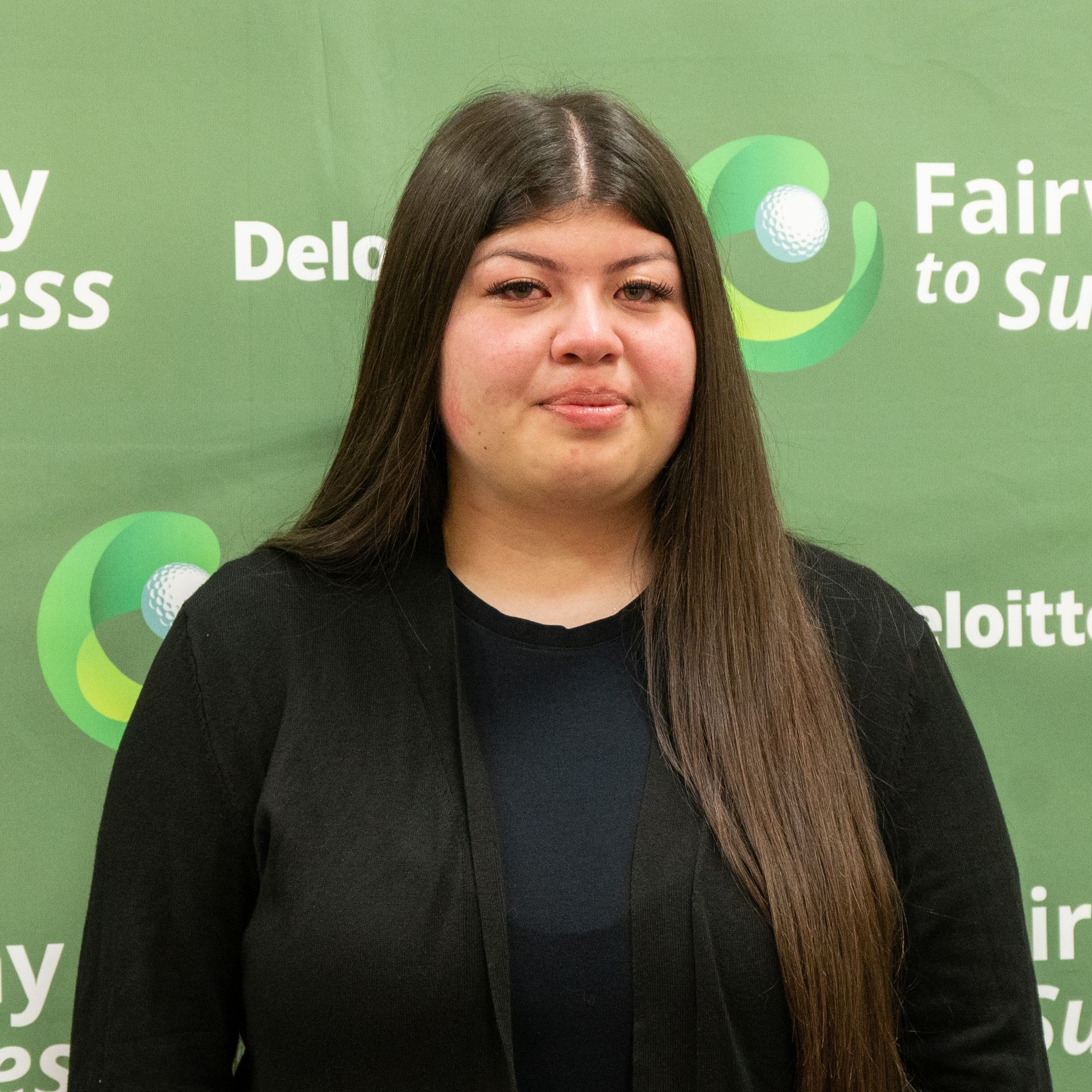 Woman in a black blazer posing before a green Deloitte backdrop with white and green logos