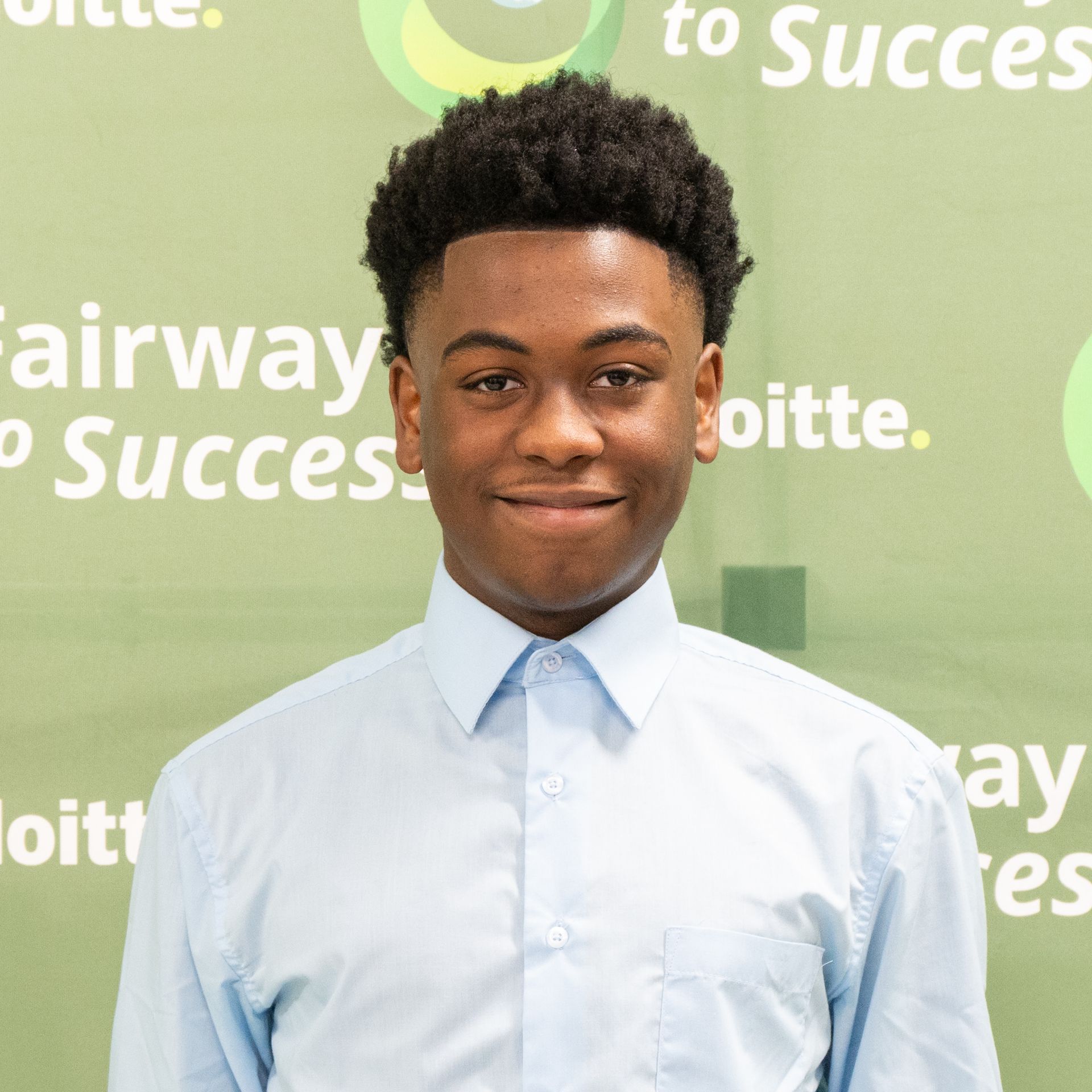Smiling person in a light blue shirt standing before a green Deloitte backdrop.