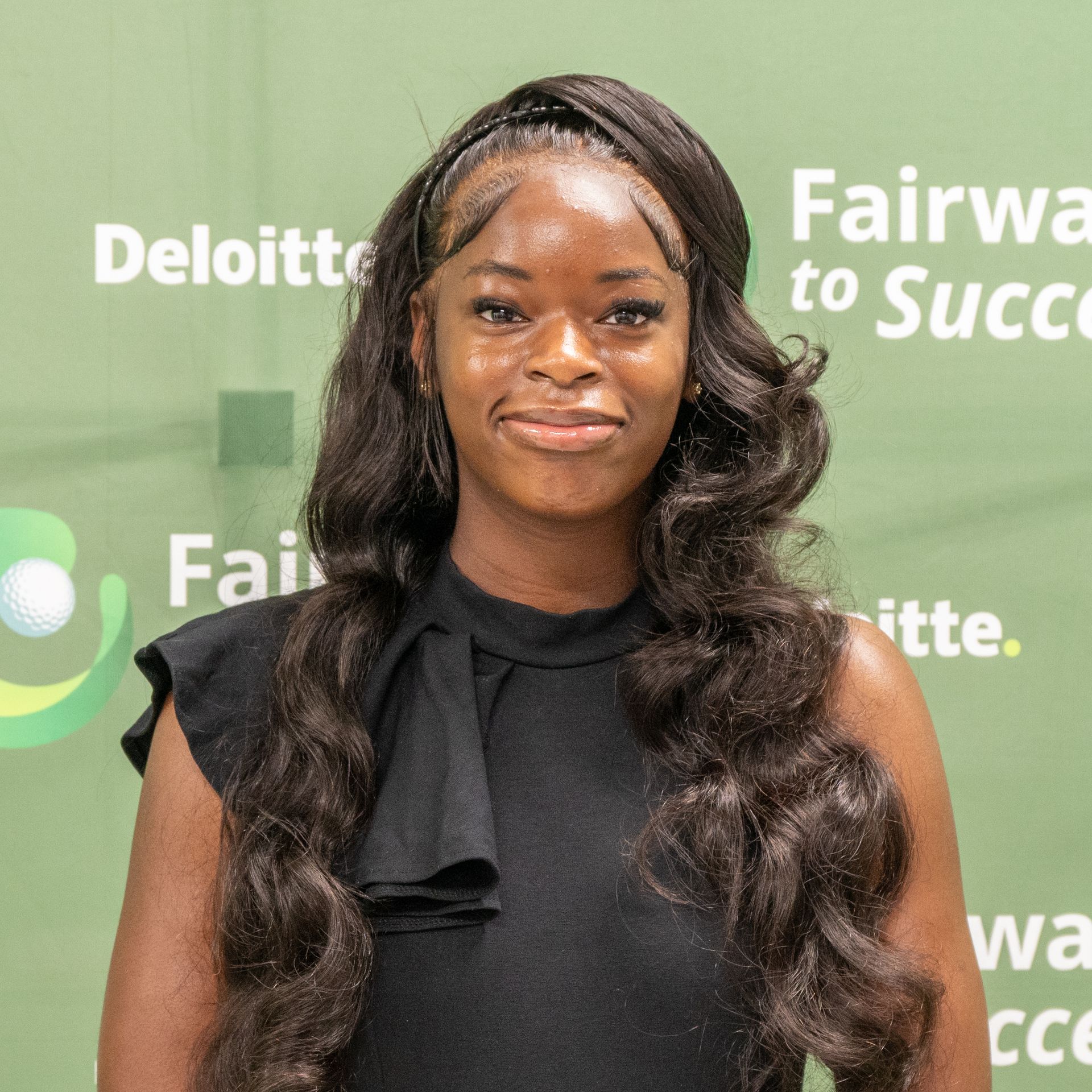 Woman in a black dress standing before a green Deloitte “Fairway to Success” backdrop