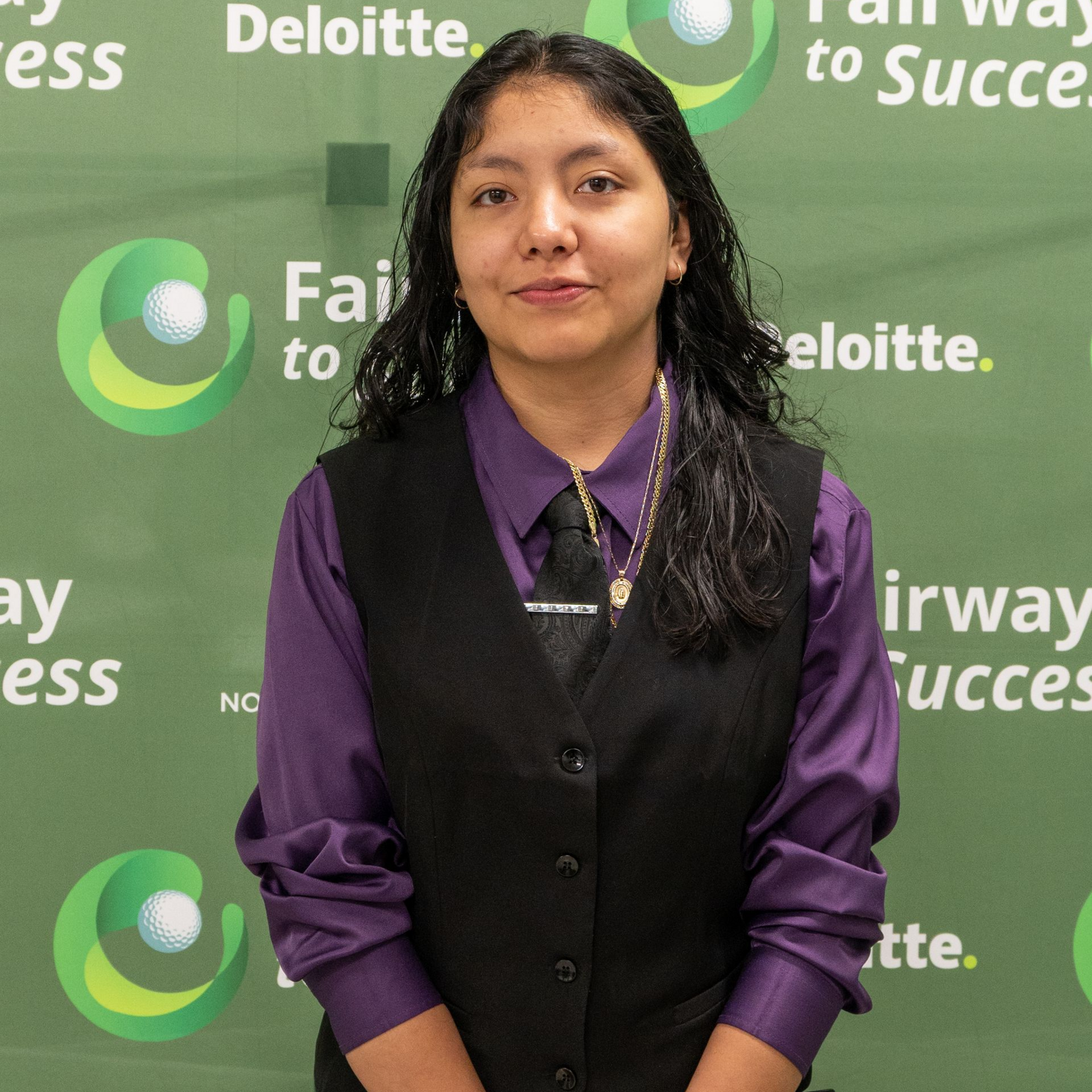 Person in purple shirt and black vest standing before a Deloitte