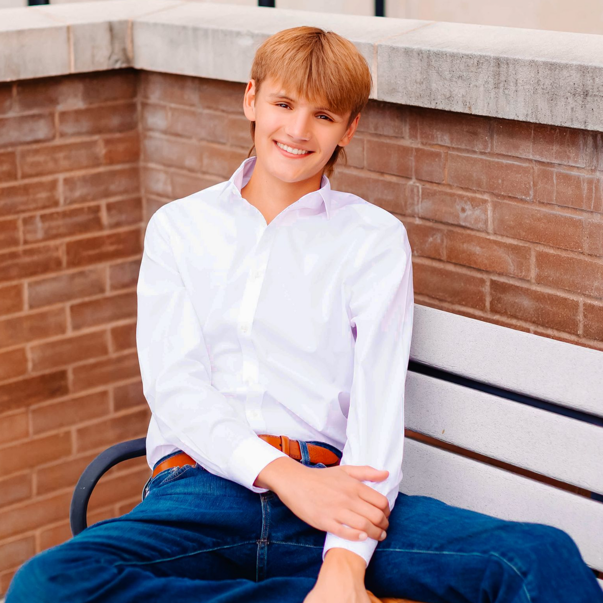 Person sitting on a bench outdoors, smiling in a white shirt and blue jeans.