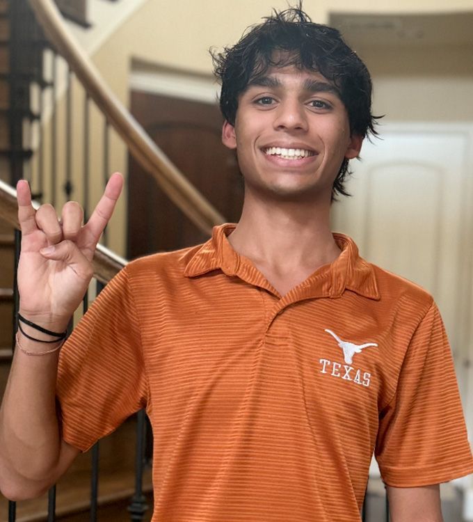 Smiling person in an orange Texas polo shirt making a hand sign indoors