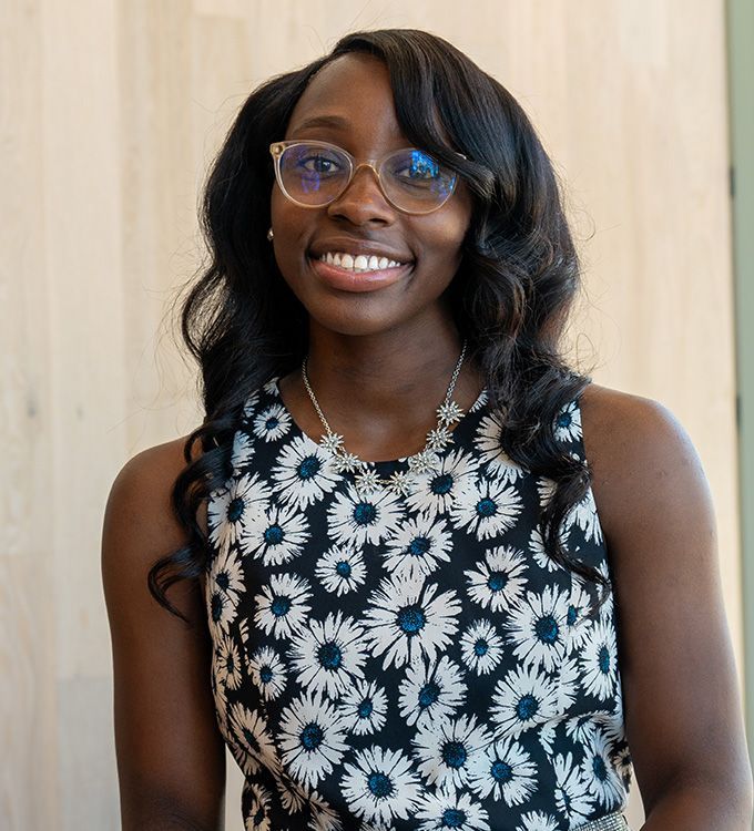 Smiling person wearing glasses and a black-and-white floral top against a light wood background