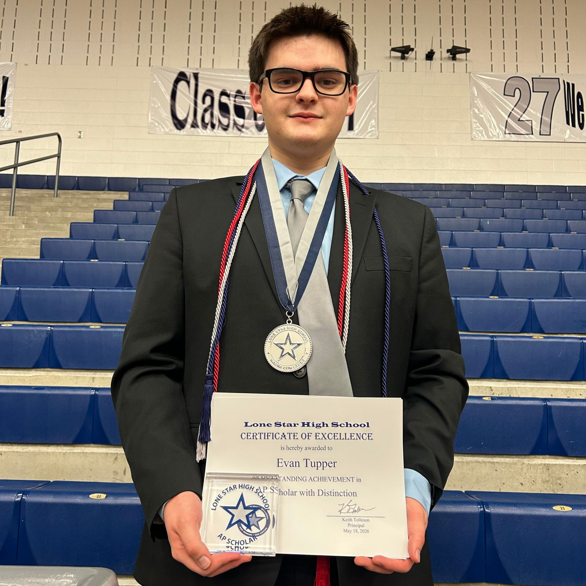 Young man in suit holding a certificate and medal in a gymnasium bleachers