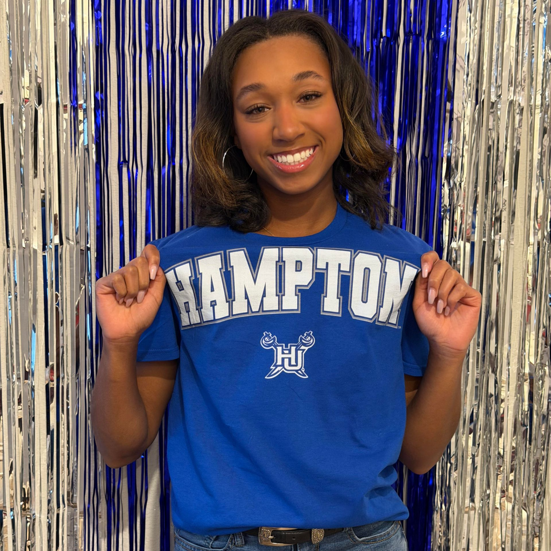 Smiling person in blue HAMPTON shirt posing in front of silver streamers