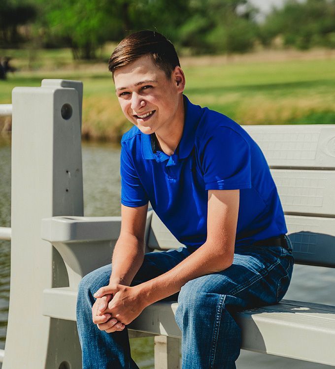 Man in a blue polo shirt sitting on a park bench outdoors, smiling in the sunlight
