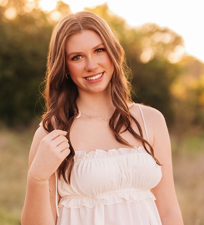 Smiling woman in a white dress standing outdoors with warm sunset light.