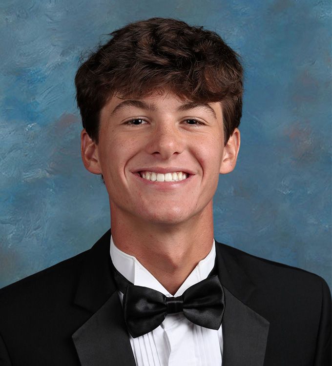 Young man in a black tuxedo and bow tie smiling against a blue studio backdrop