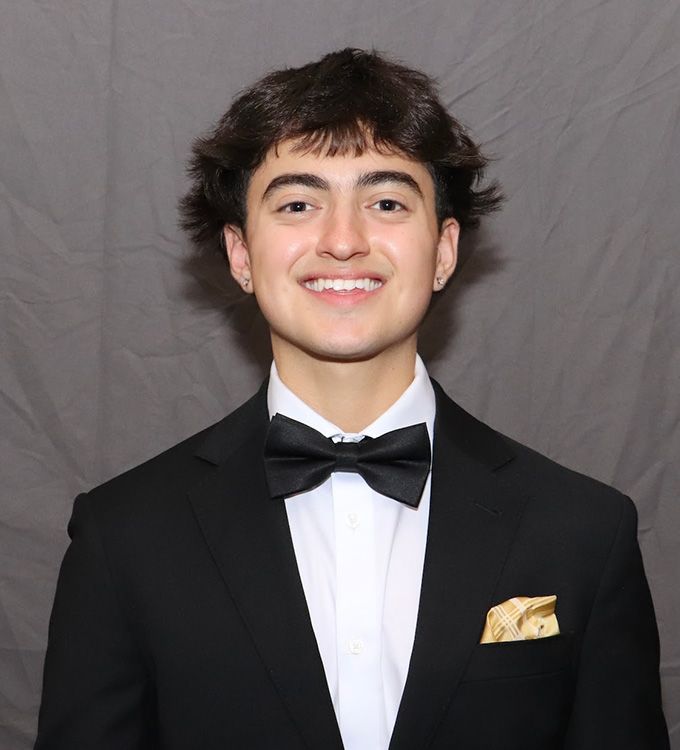 Person in a black tuxedo and bow tie smiling against a gray backdrop.
