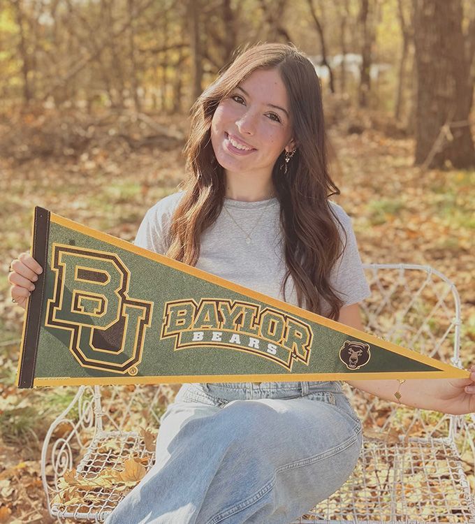 Woman holding a Baylor Bears pennant while sitting outdoors in autumn leaves