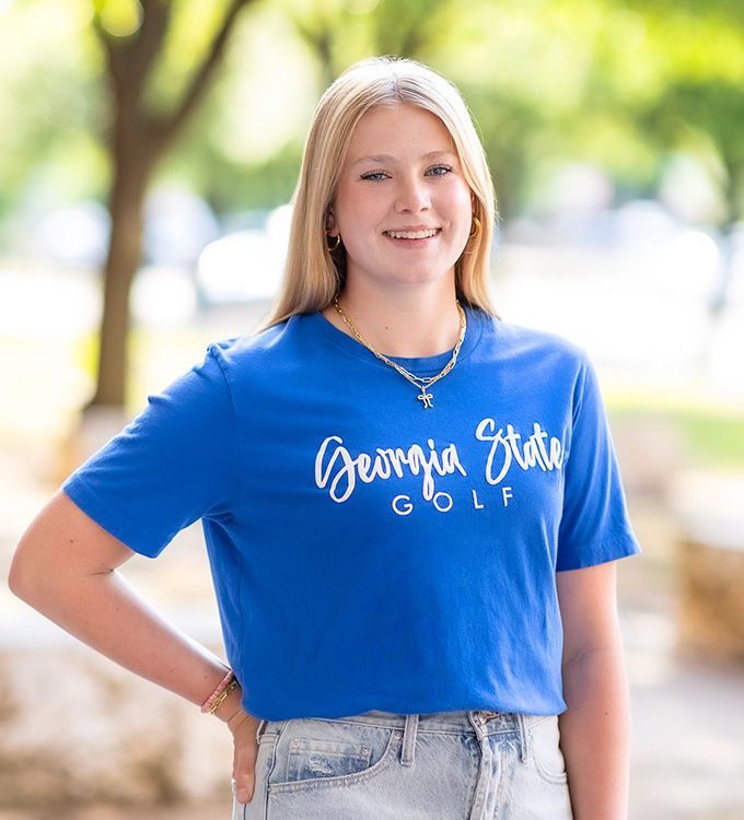 Smiling person in a blue “Georgia State Golf” T-shirt standing outdoors