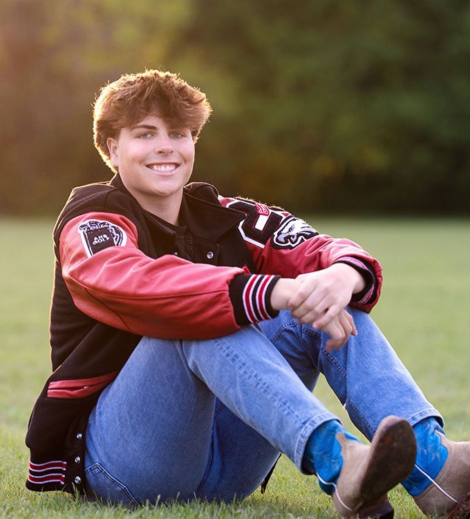 Person sitting on grass in a red-and-black jacket, smiling at the camera.