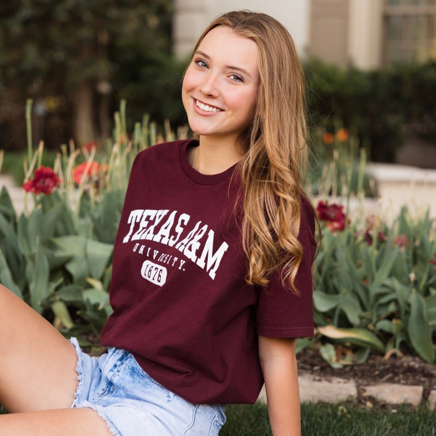 Smiling woman in a maroon Nebraska T-shirt sitting outdoors among flowers