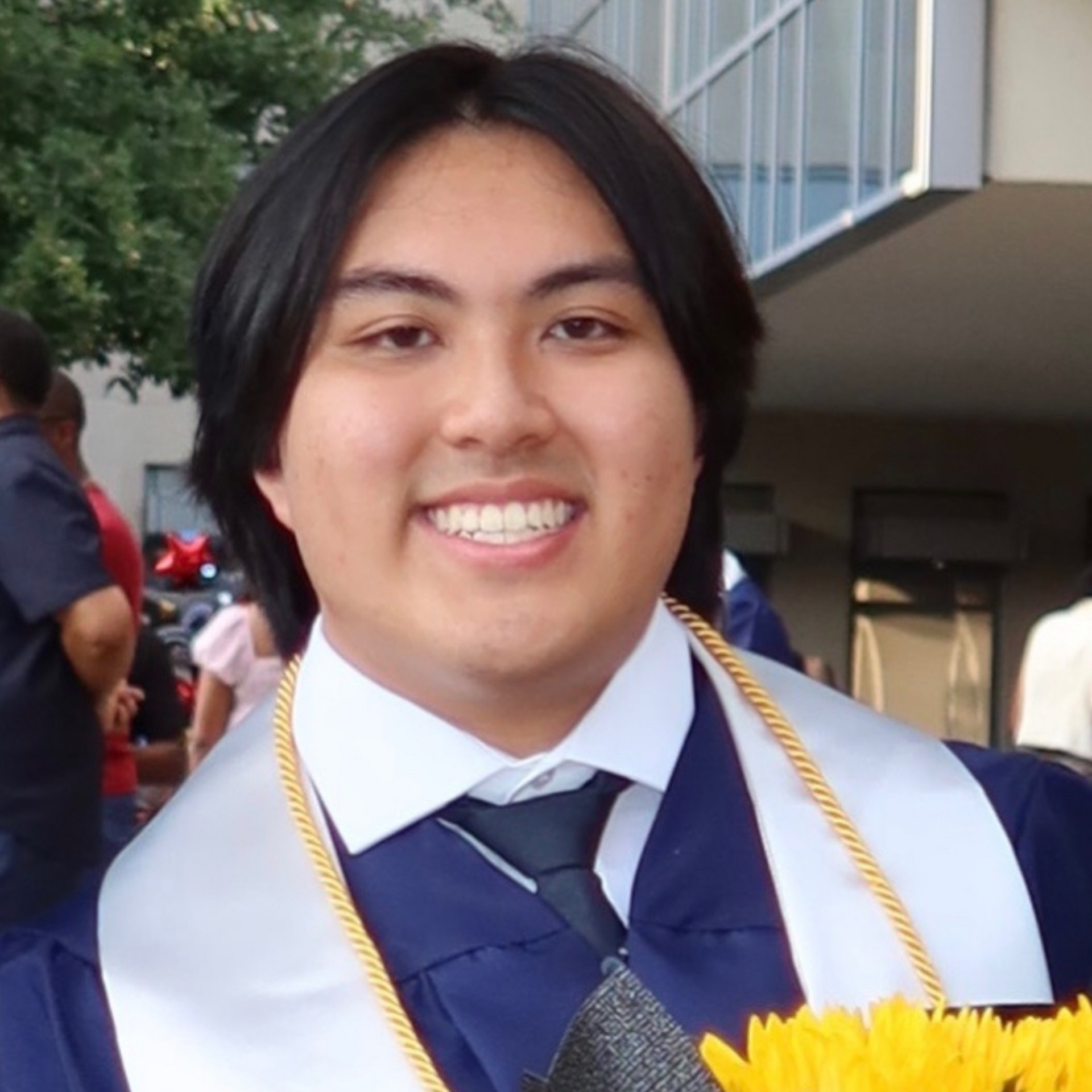 Smiling graduate in navy cap and gown with gold honor cords outdoors