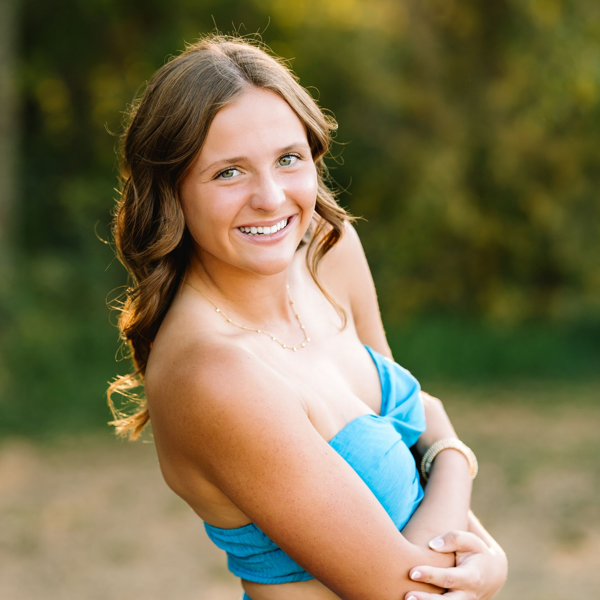 Smiling woman in a blue strapless top posing outdoors with a blurred green background