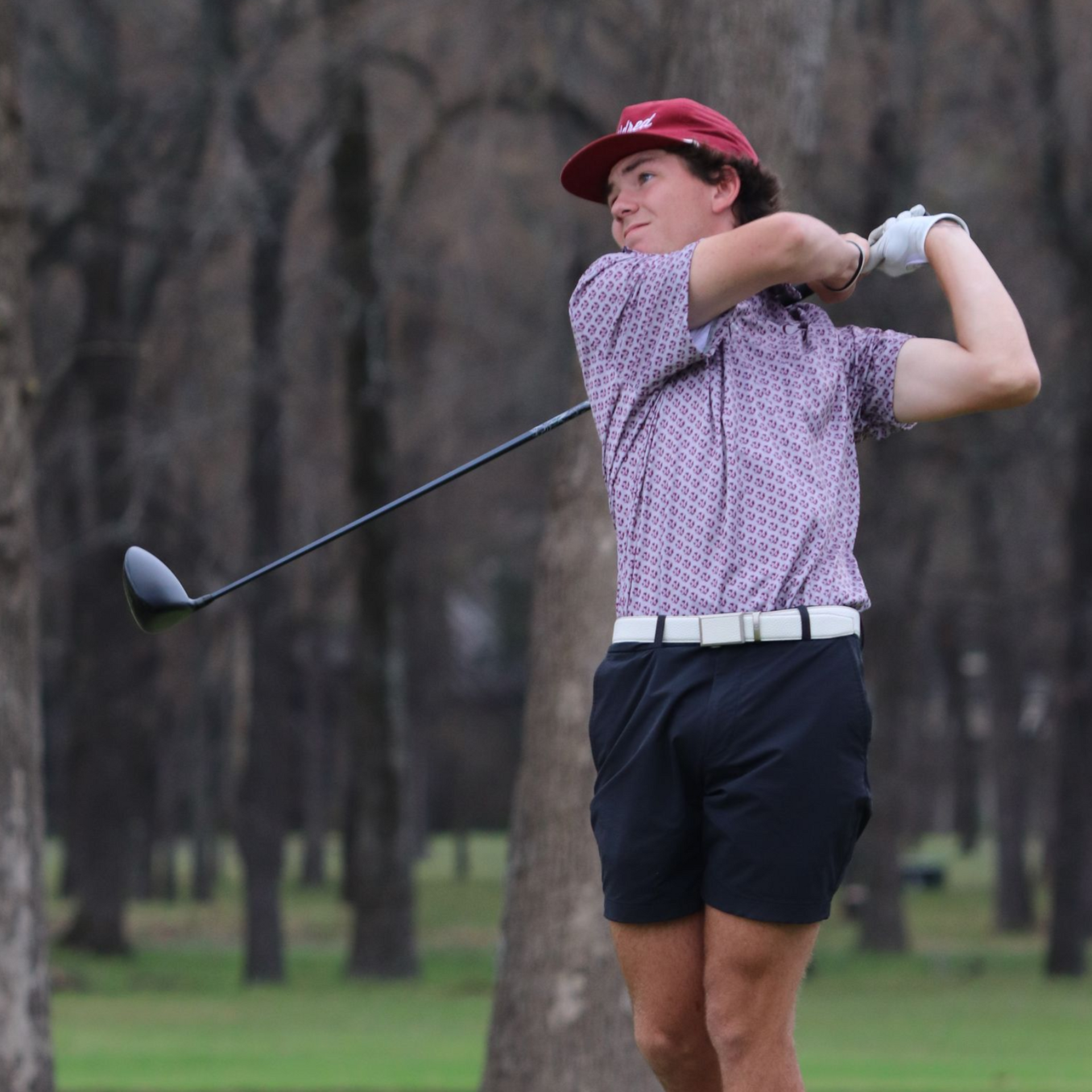 Golfer in red cap and patterned shirt finishing a swing on a golf course