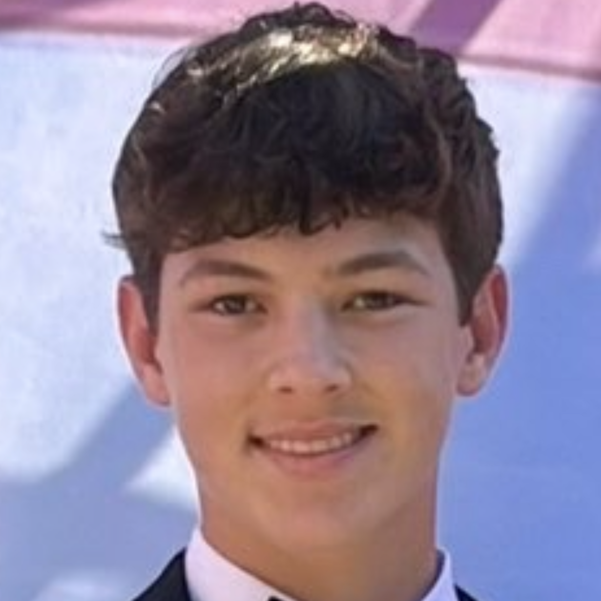 Smiling person in a light shirt and tie against a soft blue and pink background