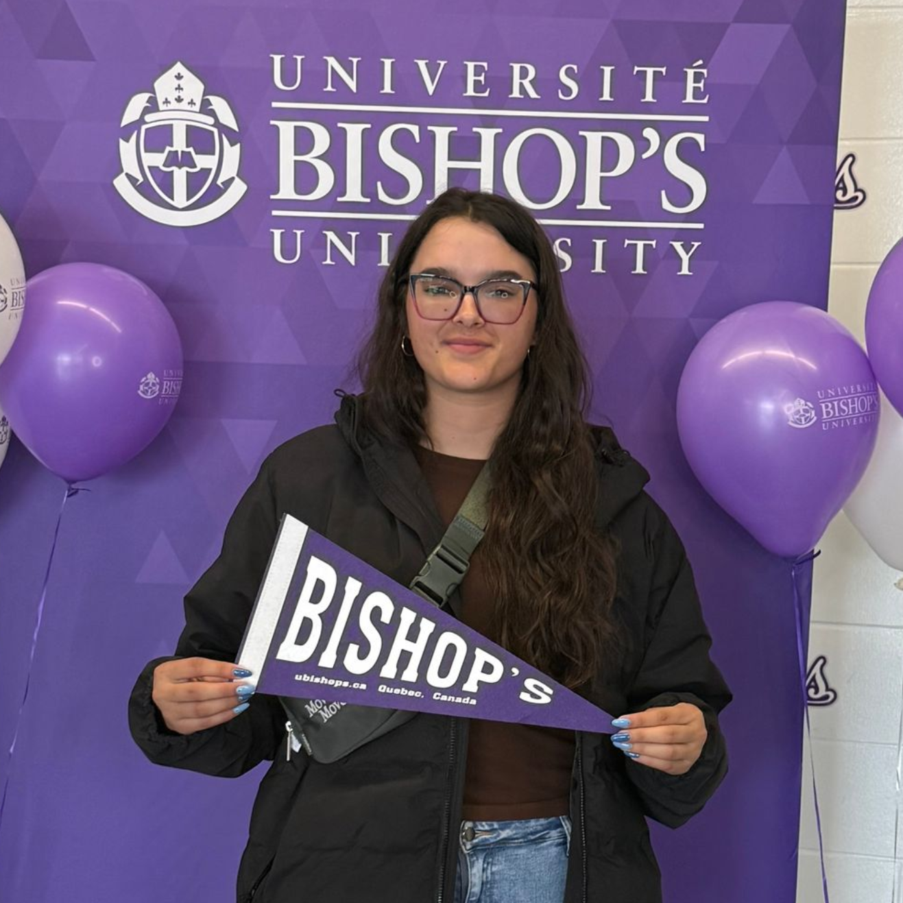 Student holding a Bishop’s pennant in front of a purple Bishop’s University backdrop and balloons