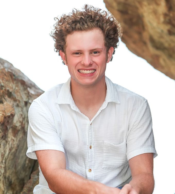 Smiling man in a white short-sleeve shirt sitting between rocks outdoors