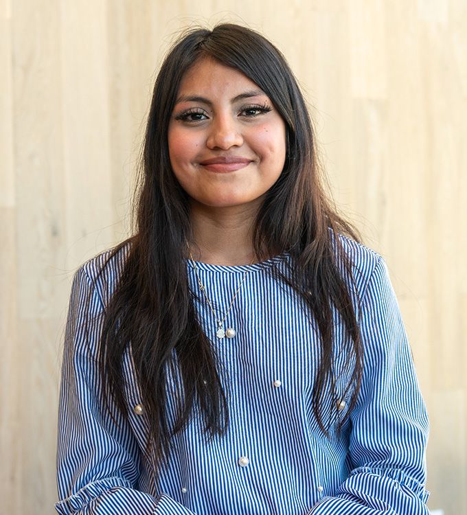 Smiling woman in a blue striped blouse standing against a light wood wall