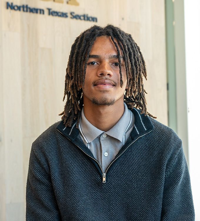 Portrait of a man with shoulder-length dreadlocks in a collared shirt and zip sweater indoors