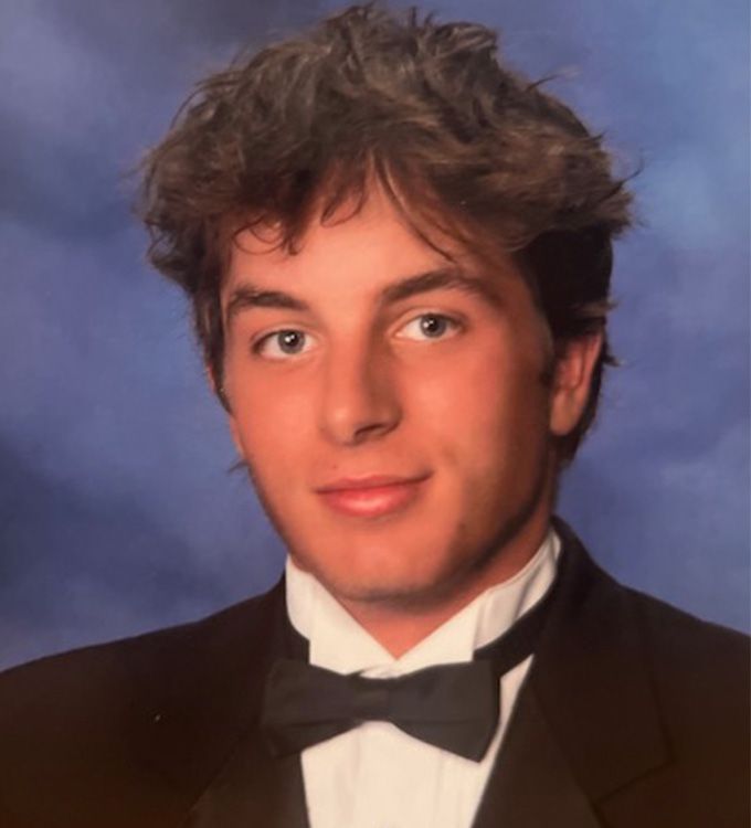 Portrait of a person in a tuxedo with a black bow tie against a blue studio backdrop
