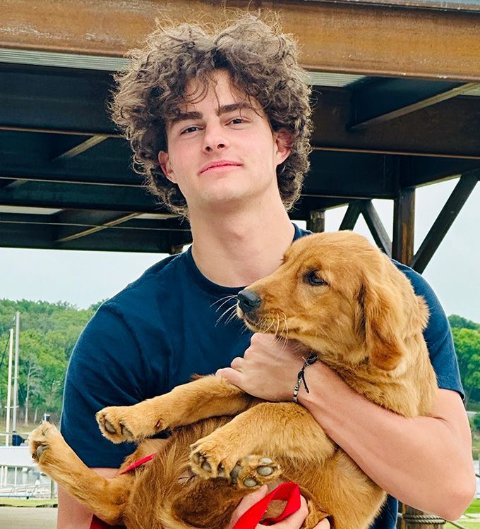Young person in a black shirt holding a golden-brown puppy under a wooden structure