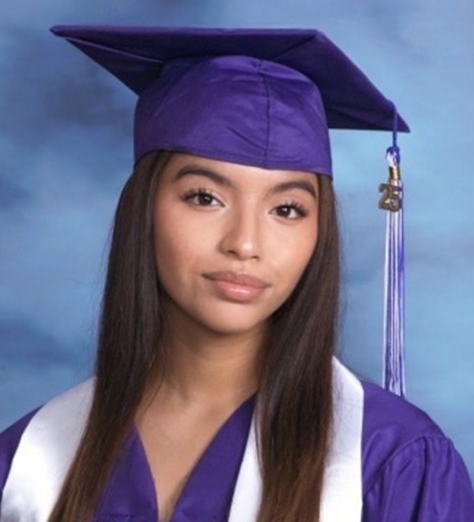 Young graduate in a purple cap and gown against a blue studio backdrop