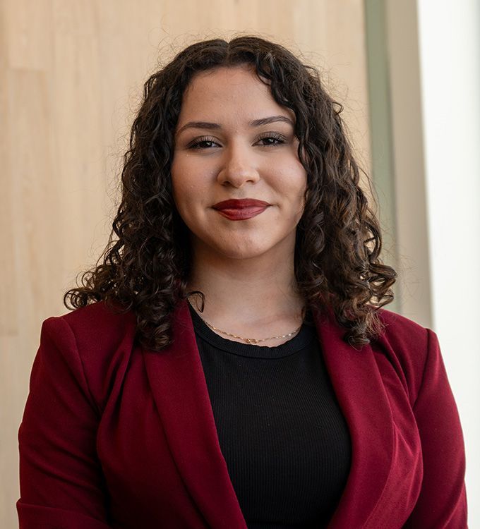Portrait of a smiling person in a burgundy blazer and black top against a light indoor background