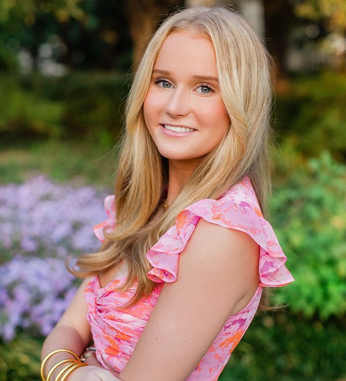 Smiling blonde woman in a pink floral dress standing outdoors in a garden