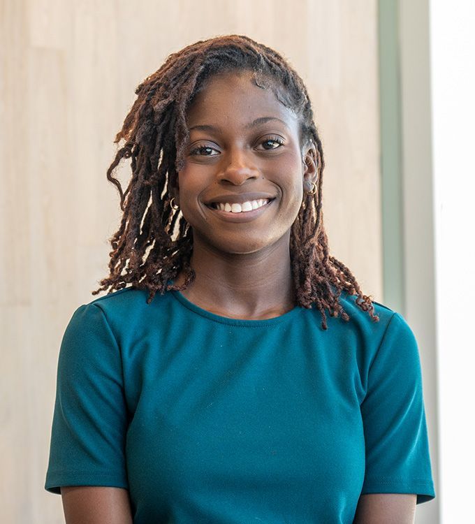 Smiling person in a teal shirt standing indoors against a light background