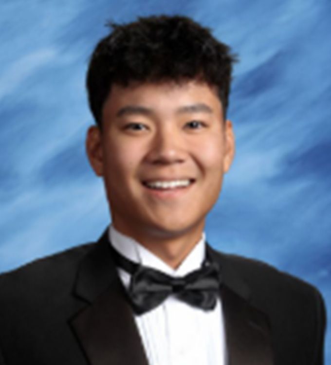 Smiling person in a black tuxedo and bow tie against a blue studio backdrop