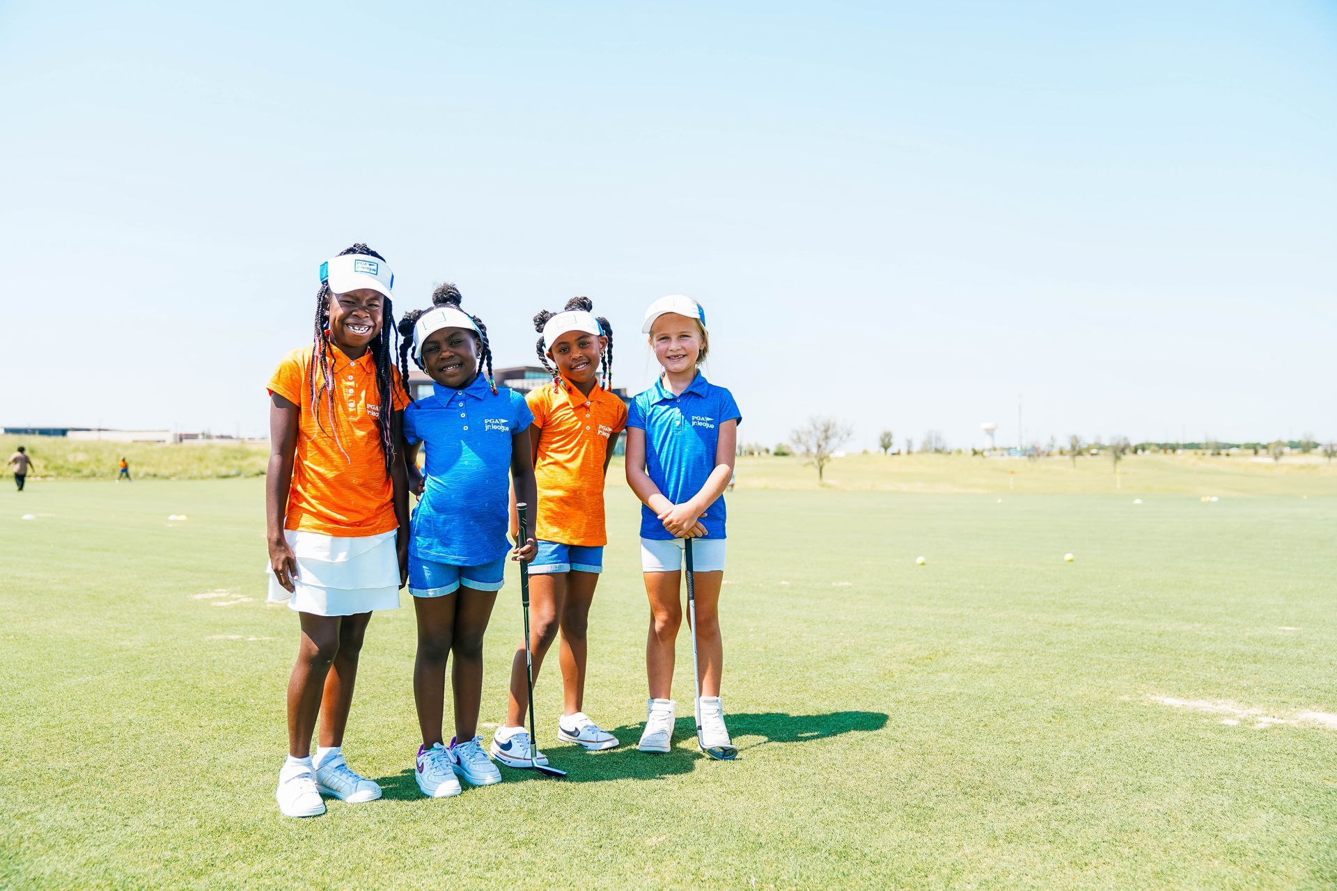 Four athletes in orange and blue sports uniforms stand together on a sunny field.