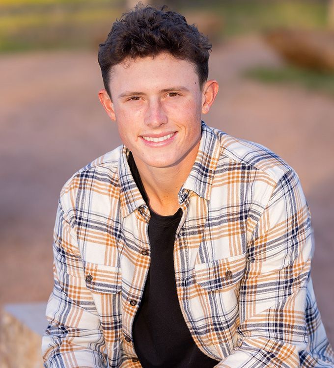 Smiling person in a plaid shirt sitting outdoors against a blurred background
