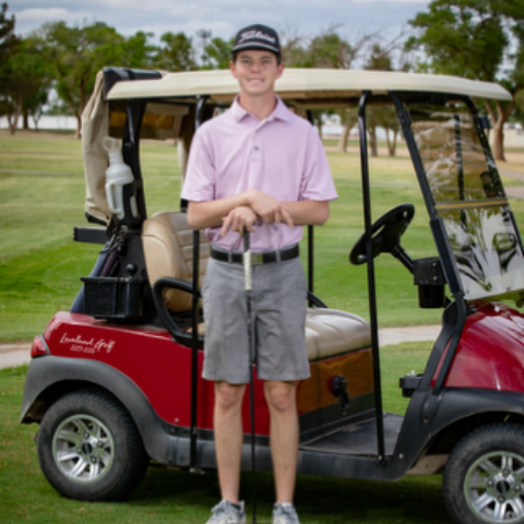 Person standing beside a red golf cart on a grassy course, wearing a pink shirt and black cap.