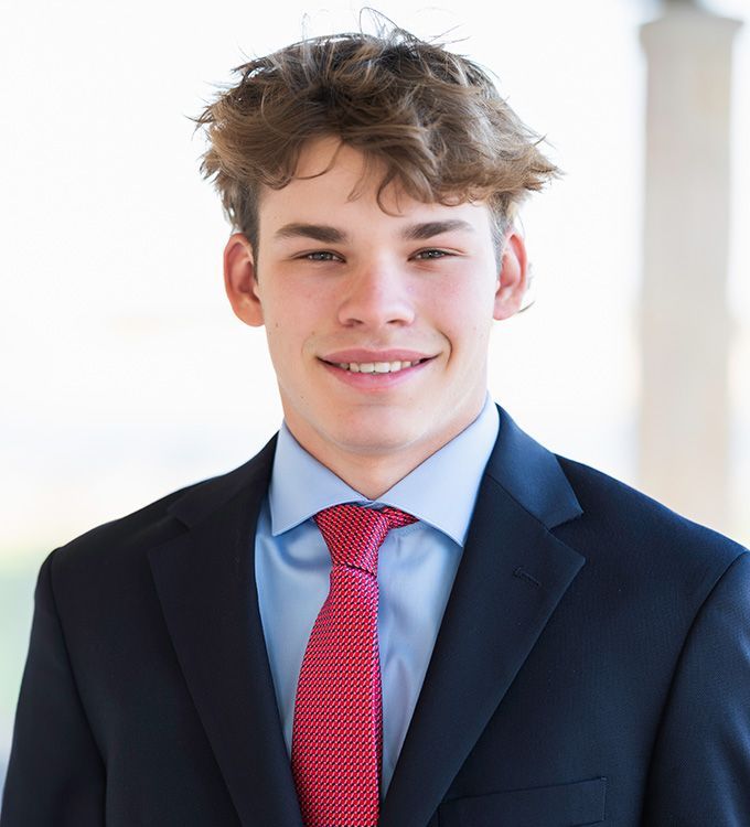 Smiling person in a navy suit and red tie against a bright indoor background