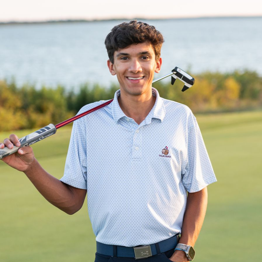 Golfer smiling on a course, holding a putter over his shoulder near a lake.