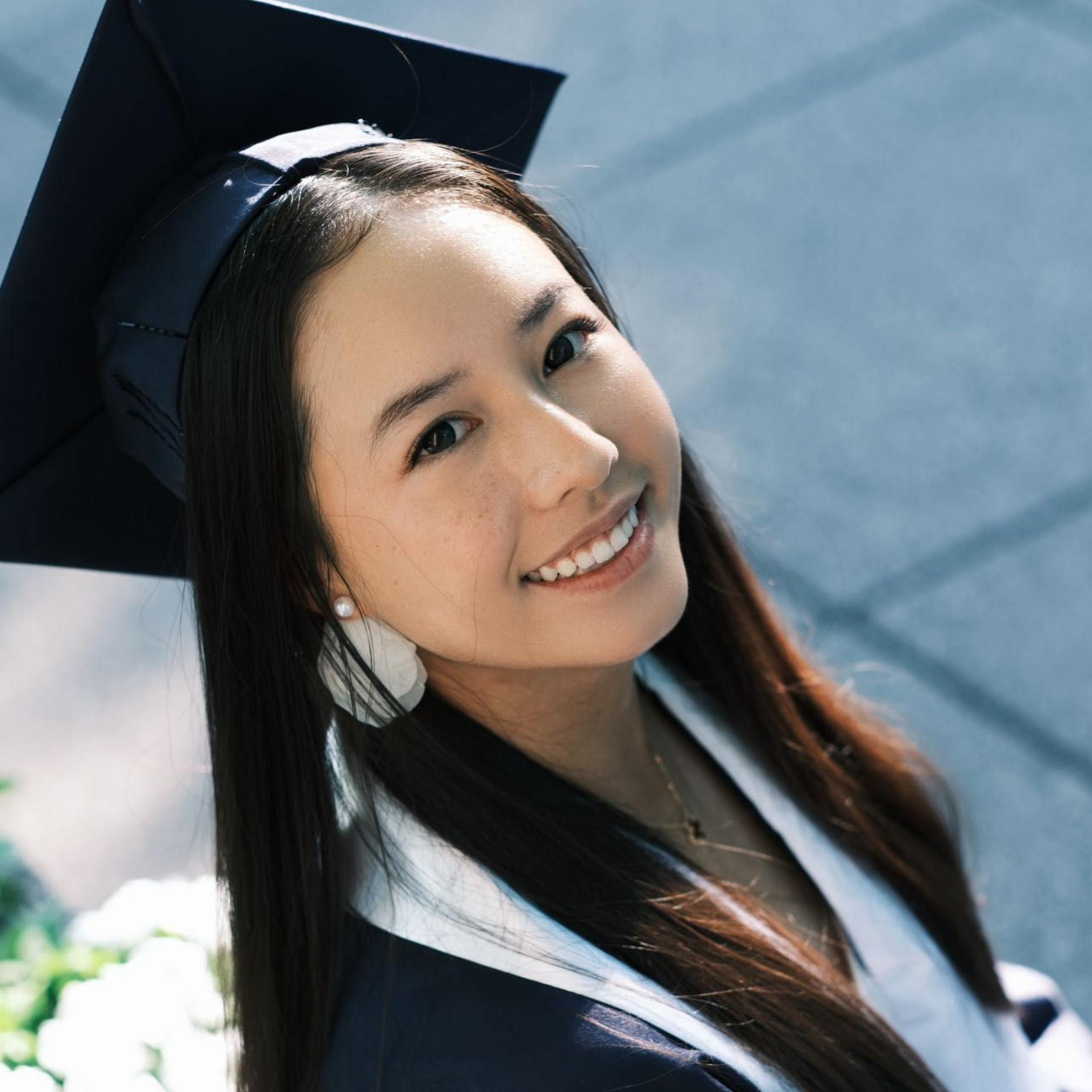 Smiling graduate in a black cap and gown, outdoors in sunlight