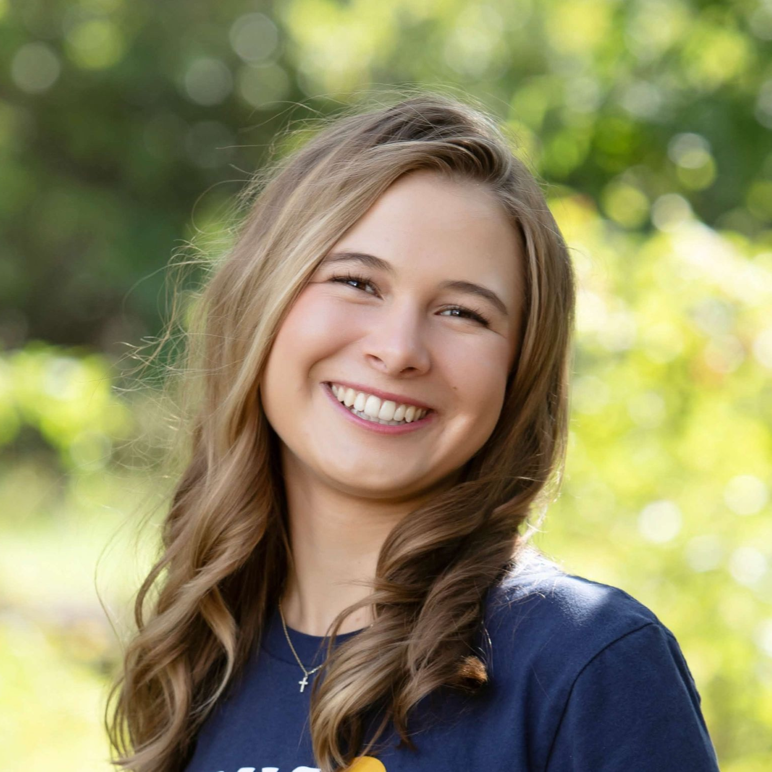 Smiling woman in a navy shirt outdoors with a blurred green background