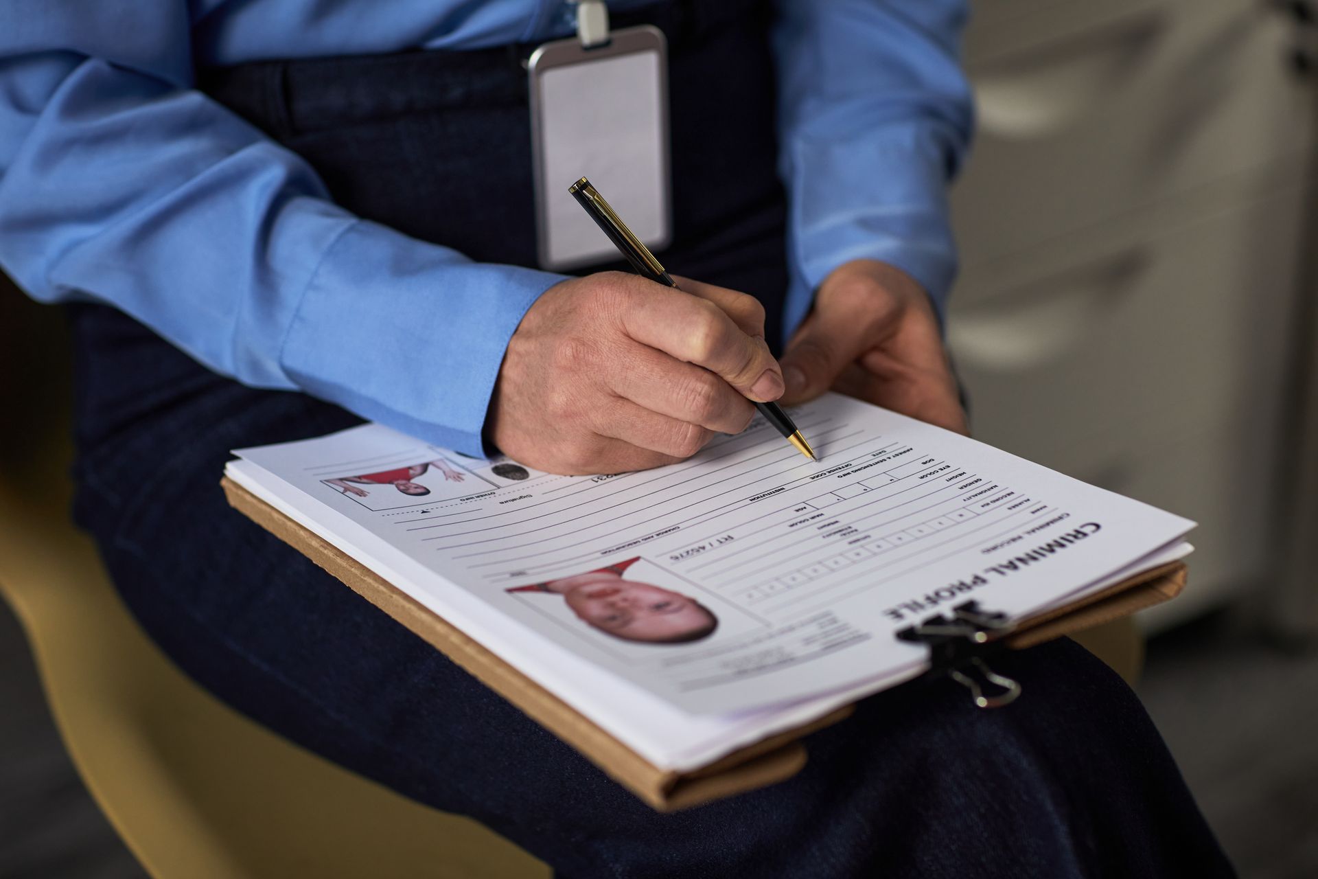 Person writing on a clipboard with a photo, wearing a blue shirt and jeans, indoors.