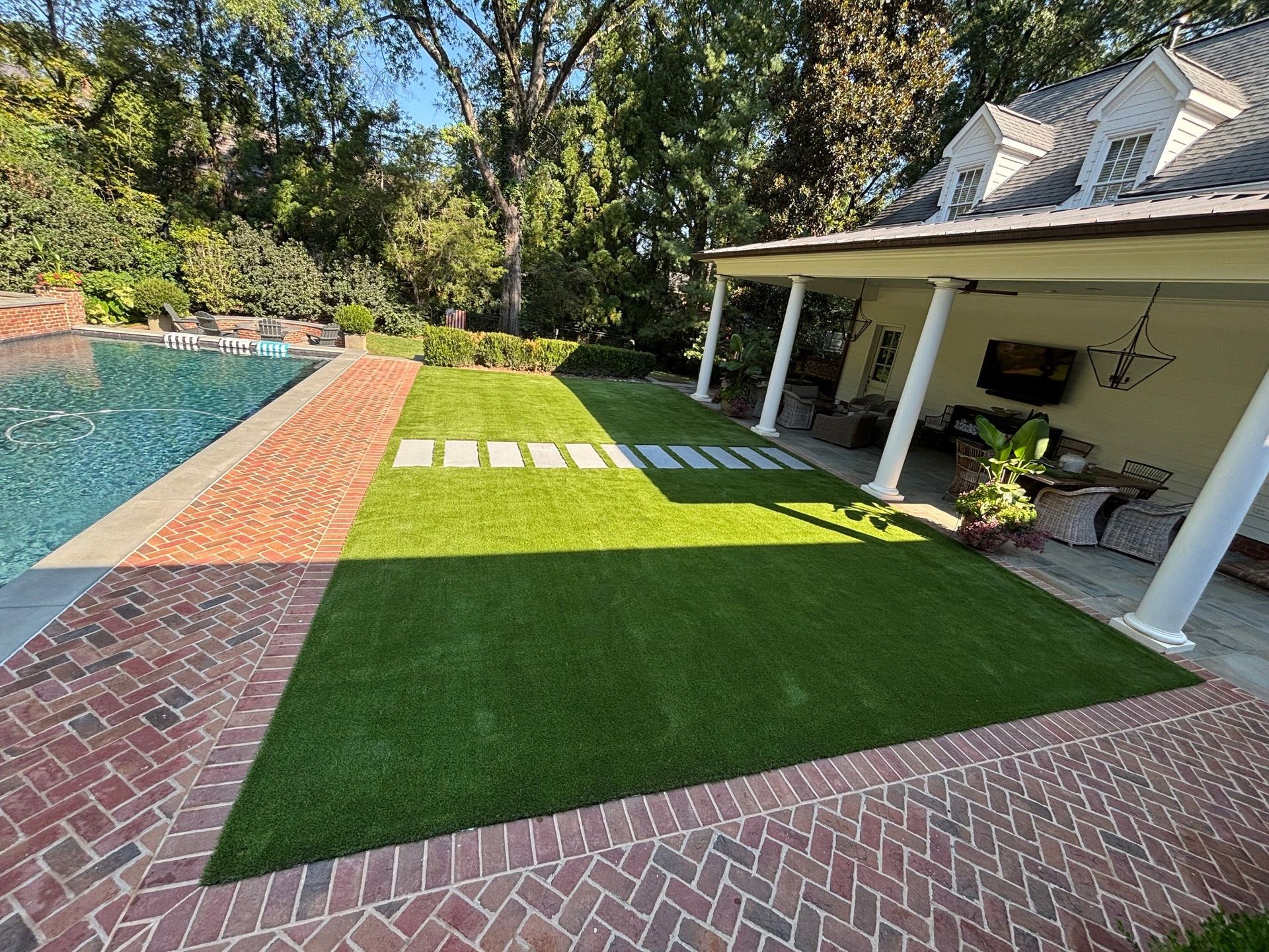 Backyard patio with pool, green lawn, stepping stones, and covered porch in bright sunlight