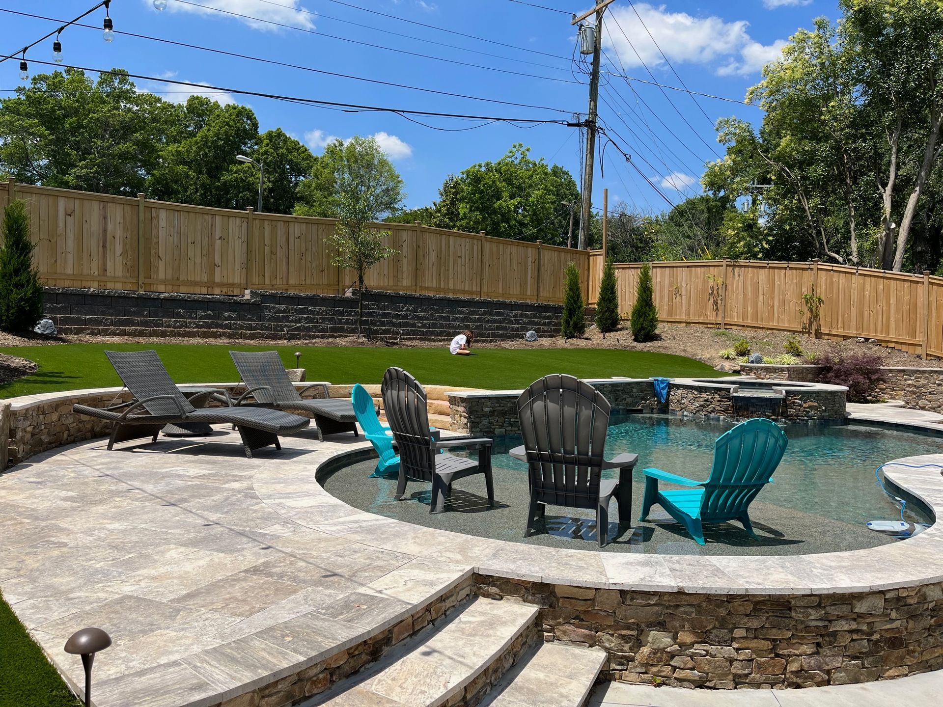 A swimming pool with chairs around it and a wooden fence in the background.