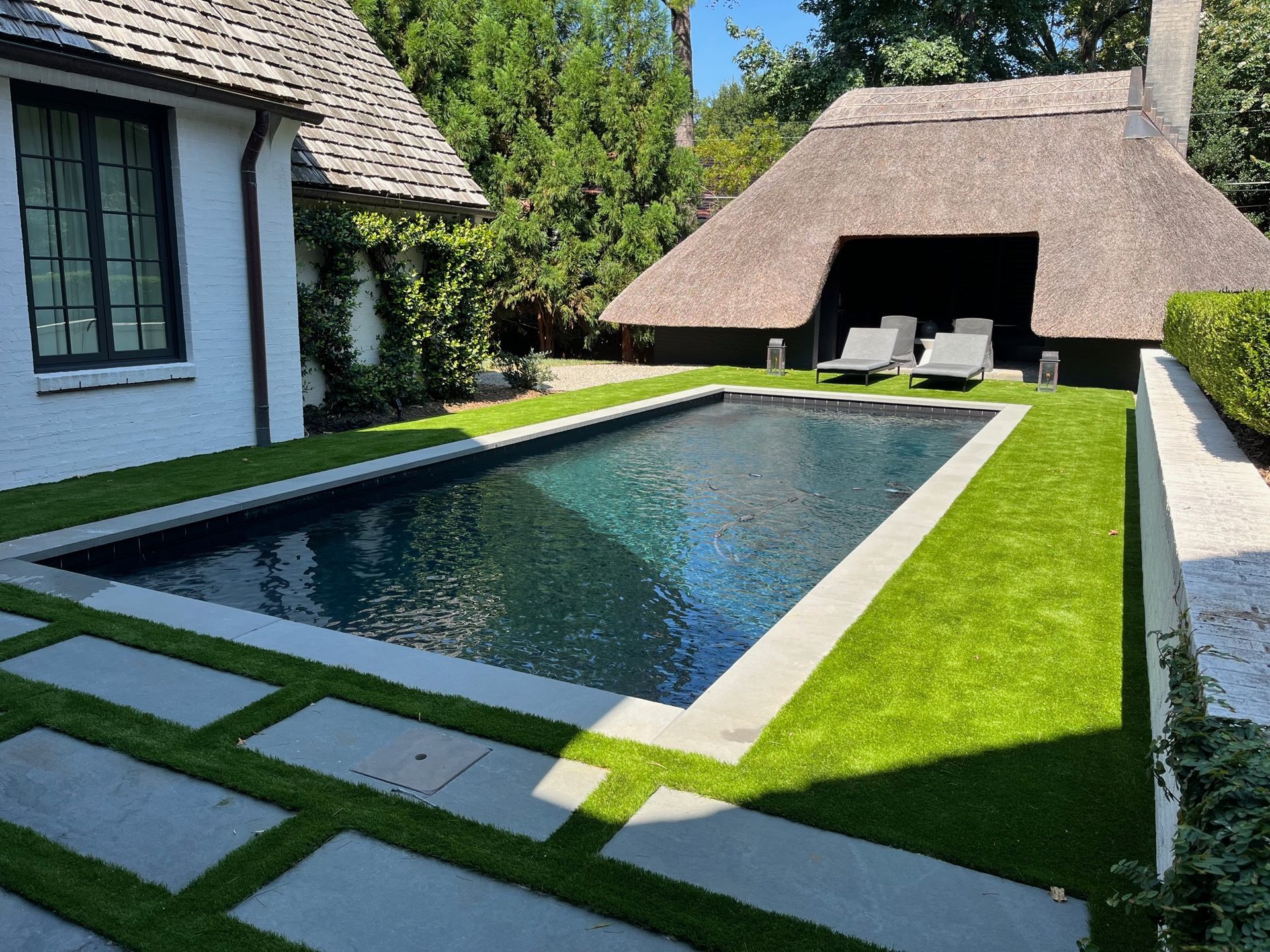 A large swimming pool in front of a house with a thatched roof