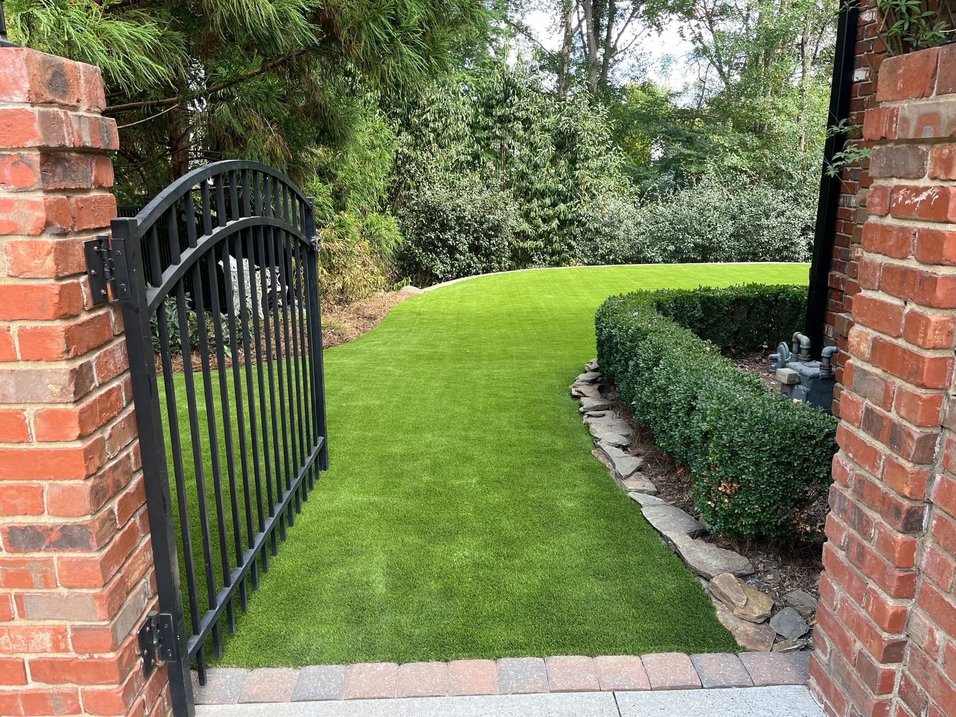 A black gate is open to a lush green lawn.