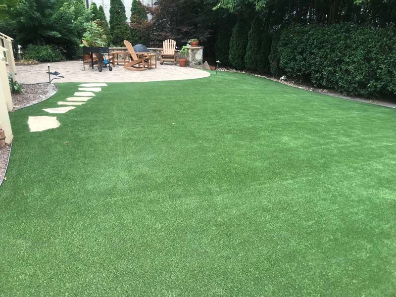 A large lawn with a patio and chairs in the background.
