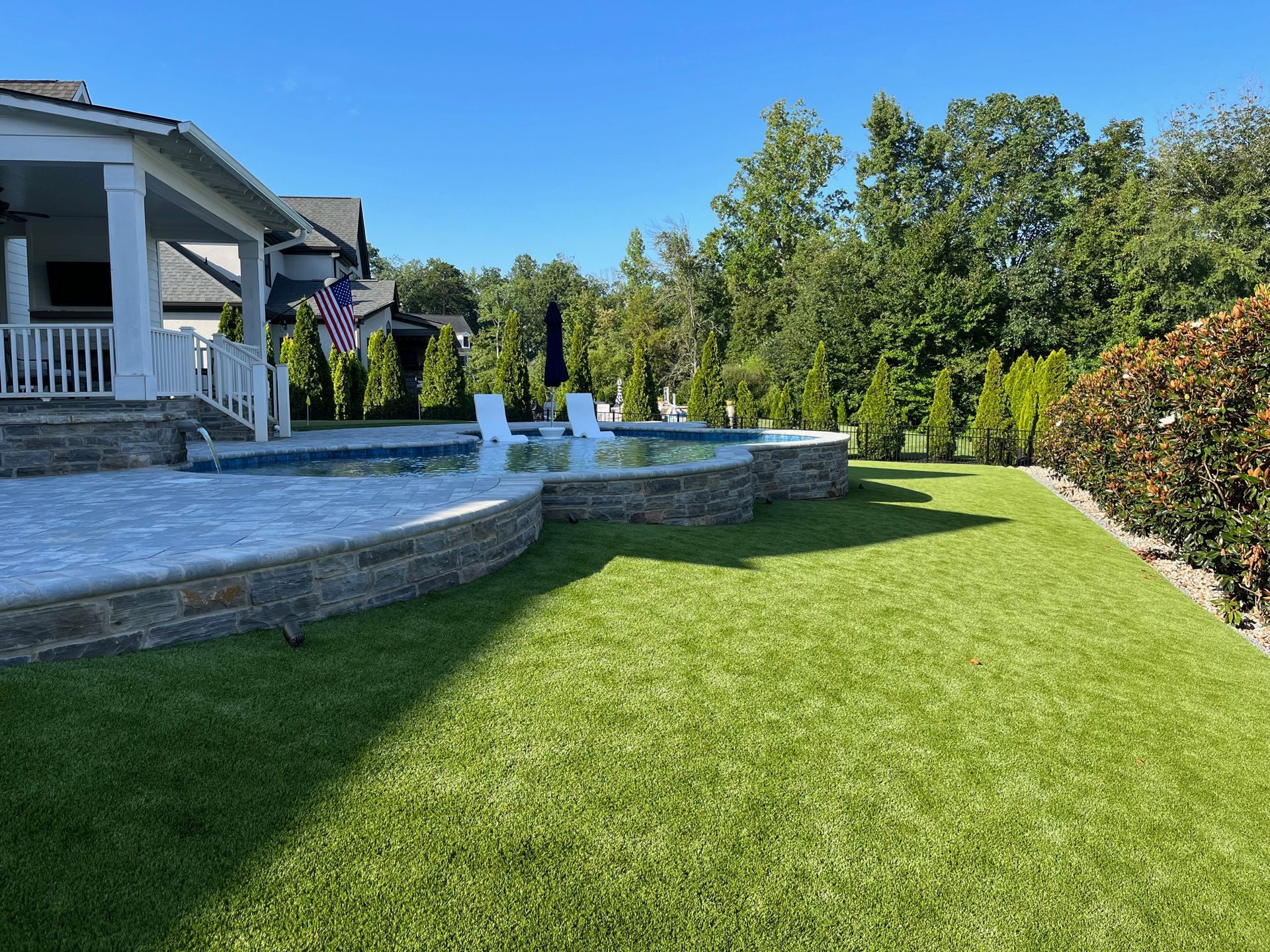 There is a large lawn in front of a house with a pool.